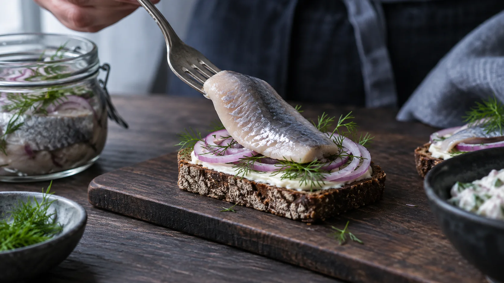 En sildefilet lægges på et stykke rugbrød med en gaffel.